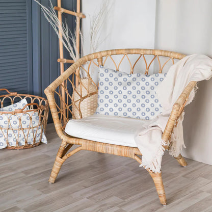 Wicker chair with a patterned pillow and white blanket in a room with a basket and decorative items.