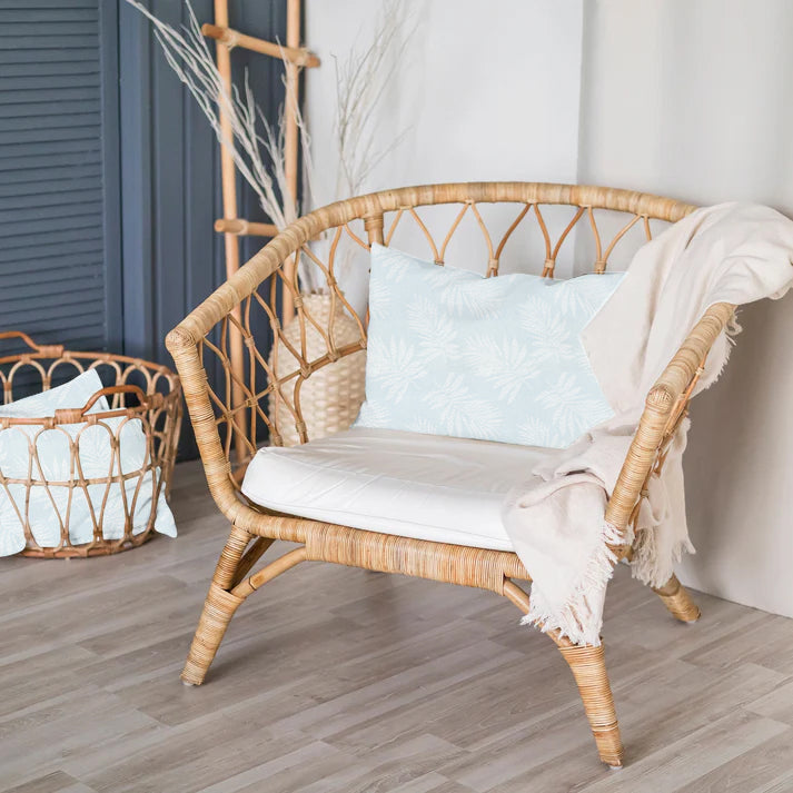 Wicker chair with white cushion and blanket in a room with a basket and decorative items.