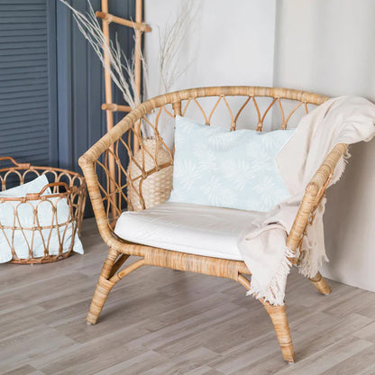 Wicker chair with white cushion and blanket in a room with a basket and decorative items.