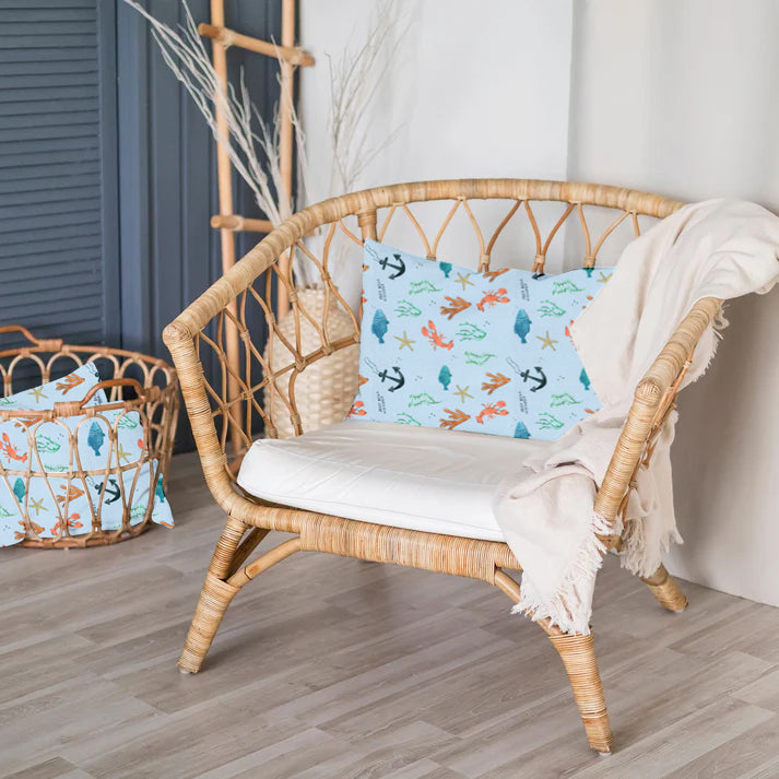 Wicker chair with a decorative pillow featuring sea-themed designs in a room setting.