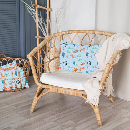 Wicker chair with a decorative pillow featuring sea-themed designs in a room setting.