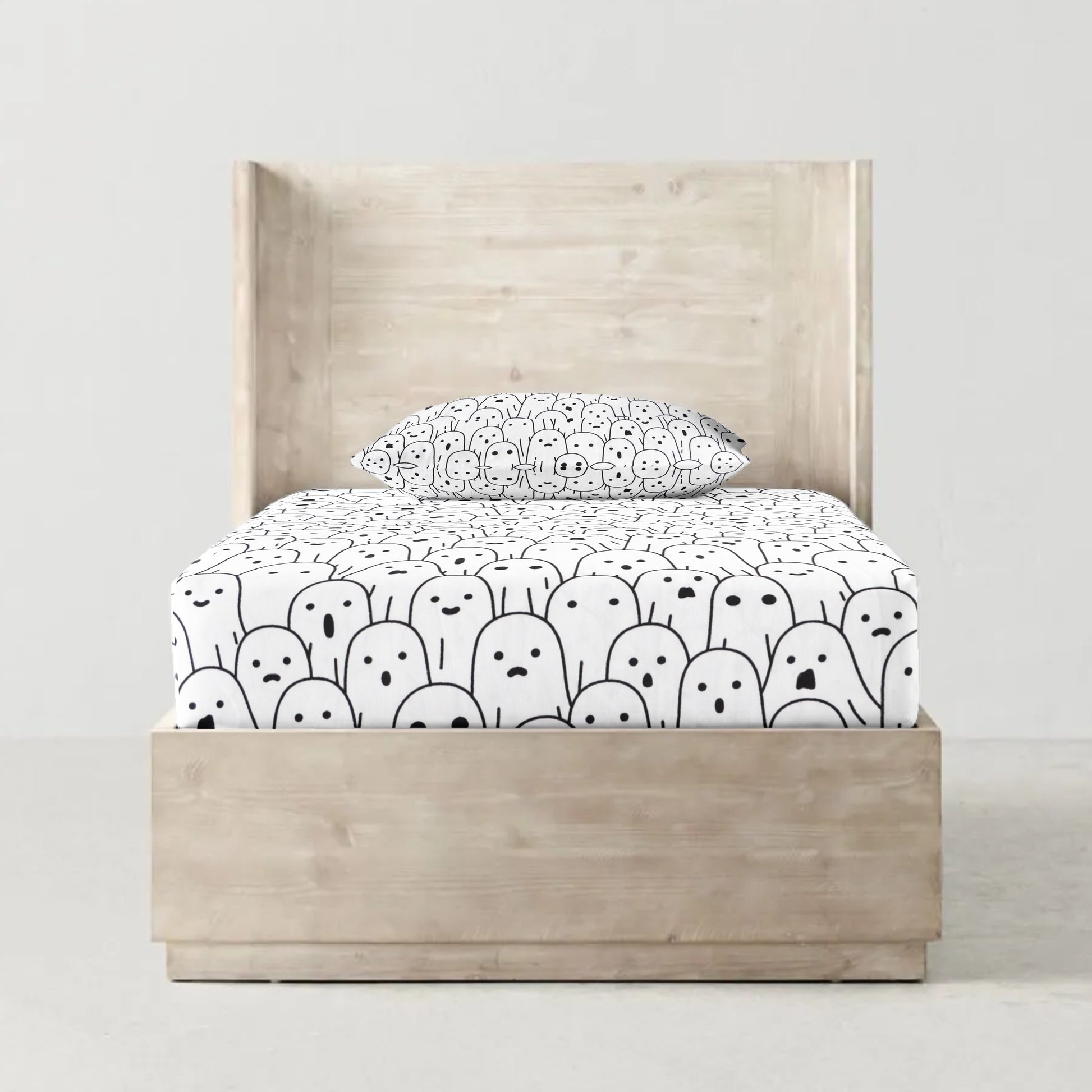 A fitted bed sheet with a black and white character pattern, displayed on a bed with a pillow on top.