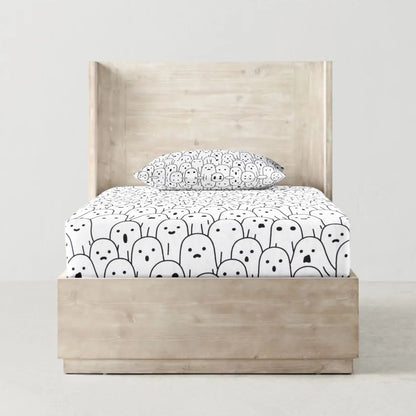 A fitted bed sheet with a black and white character pattern, displayed on a bed with a pillow on top.