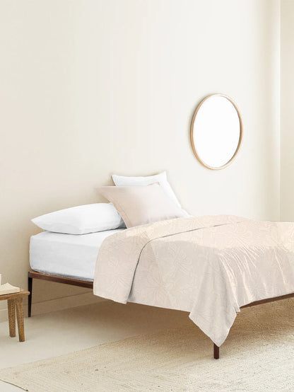 Neatly made bed with beige bedding and pillows in a minimalistic bedroom.
