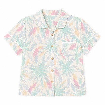 A short-sleeve button-up shirt with a pastel tropical palm leaf pattern in mint green, pink, and peach on a cream background, featuring a collar and a chest pocket.