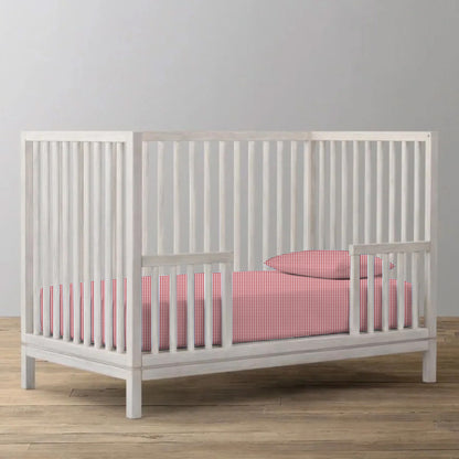 White crib with red and white checkered bedding on a wooden floor.