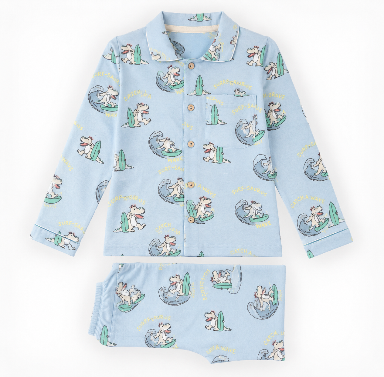 A two-piece children's pajama set laid flat on a white background, featuring a light blue long-sleeve button-front top and matching shorts with an all-over cartoon dog surfing pattern.