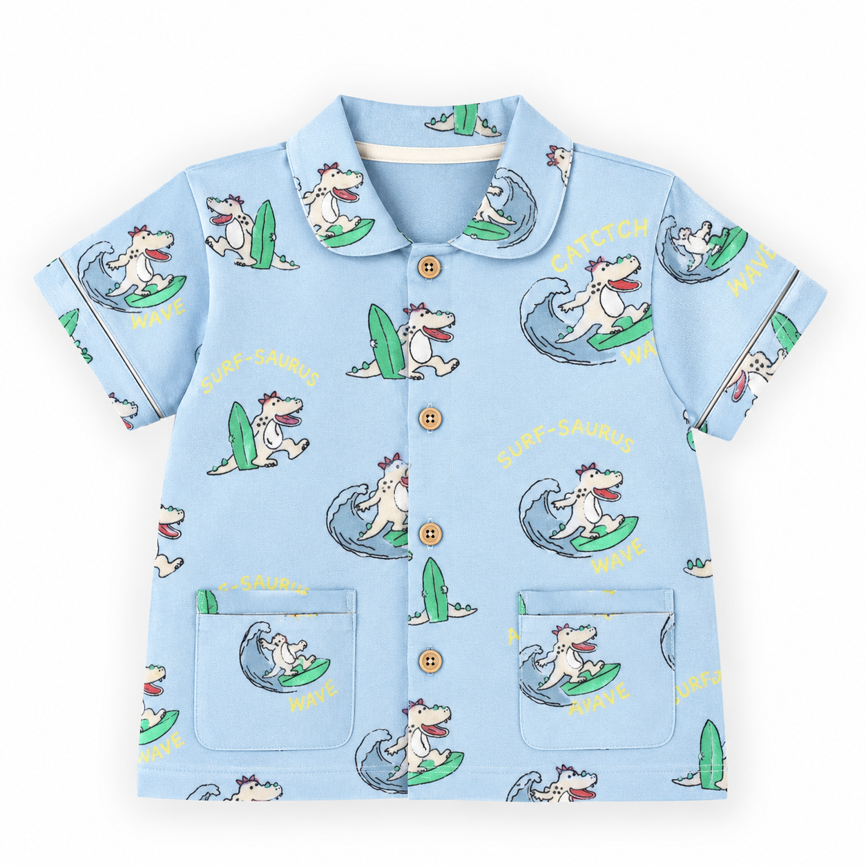 A light blue short-sleeve button-up shirt with an all-over cartoon dog surfing print, featuring a collar, gold buttons, and two front patch pockets on a white background.