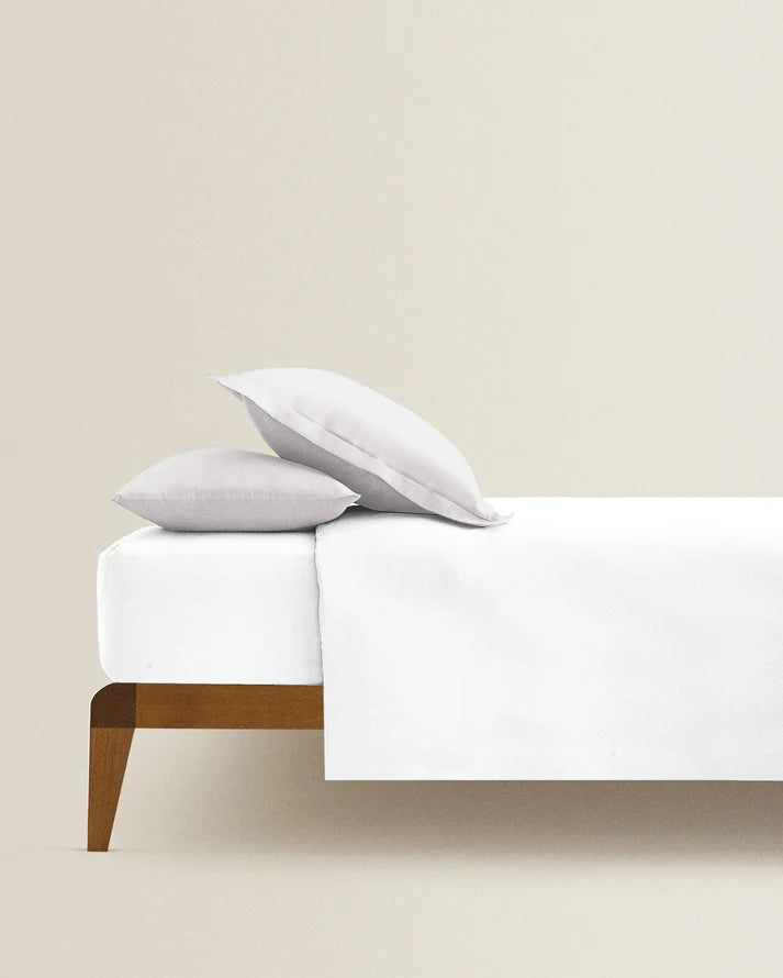 Bed with white bedding and pillows against a beige wall