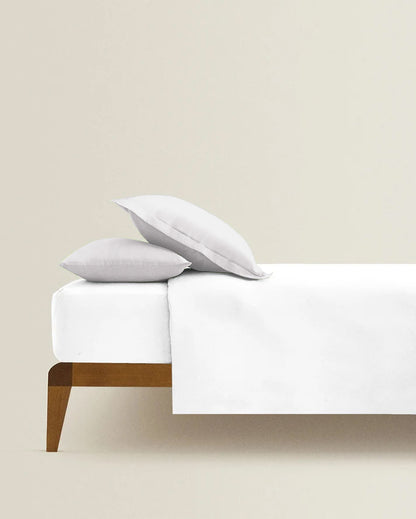 Bed with white bedding and pillows against a beige wall