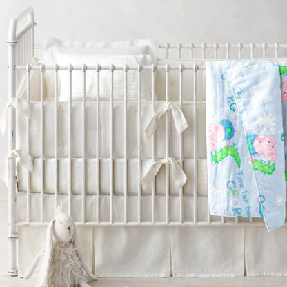 A receiving blanket with a Peppa Pig character pattern is draped over a crib with a pillow, a plush toy, and a framed picture of a sheep in the background.